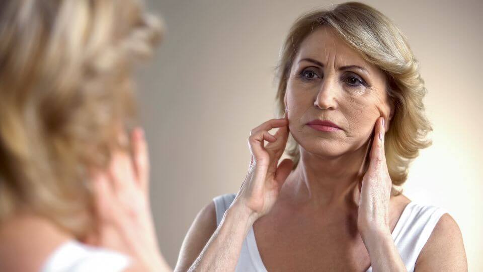 Mature caucasian woman with ageing skin looks at her reflection